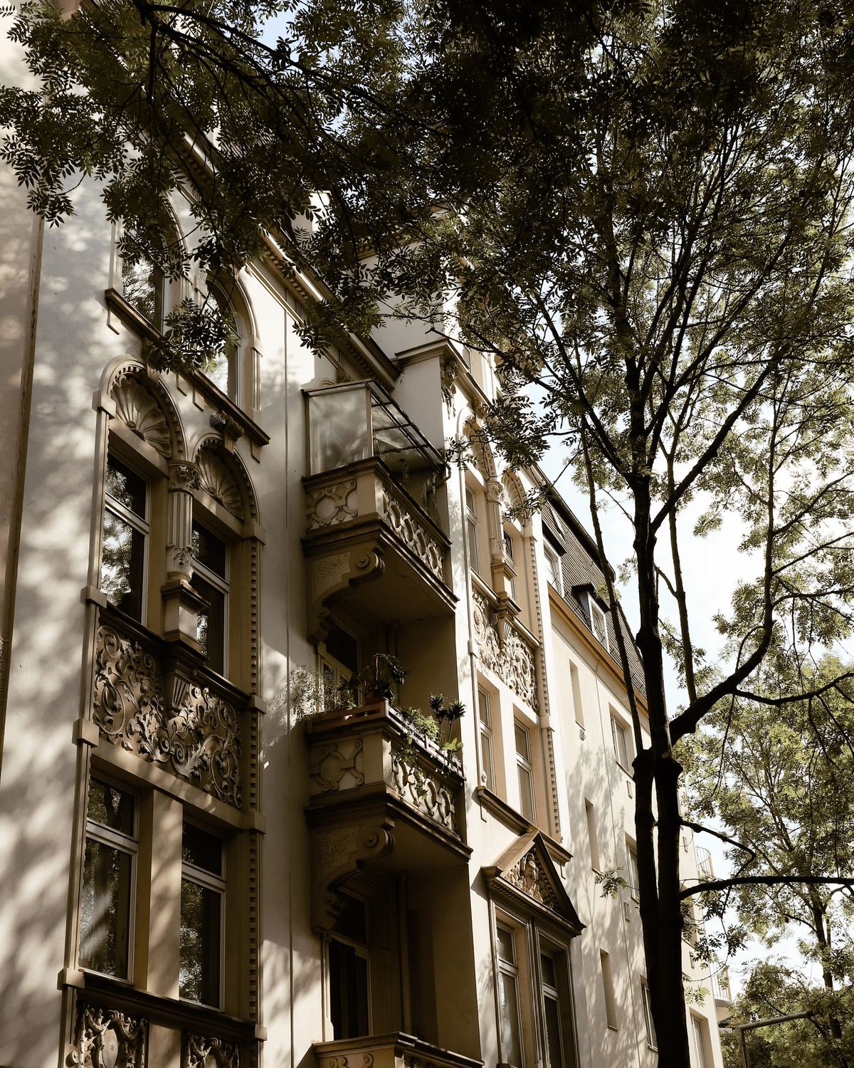 Altbau mit verzierten Balkonen hinter Bäumen
